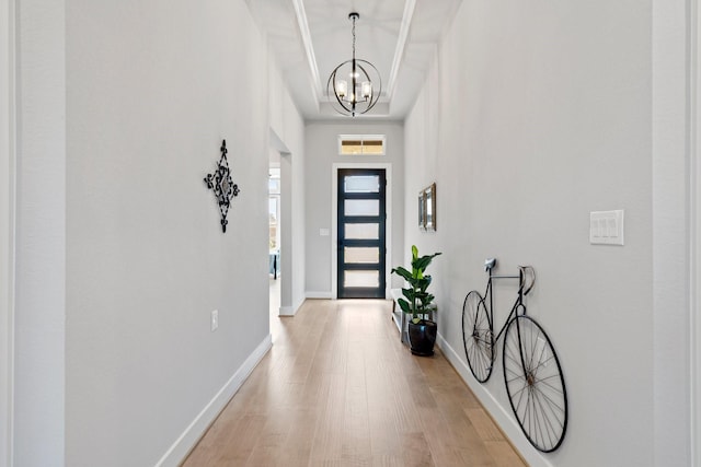 foyer entrance featuring a towering ceiling, baseboards, a notable chandelier, and light wood-style floors