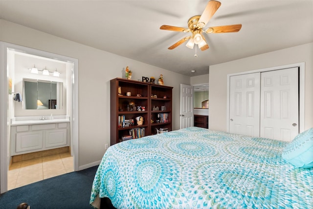 tiled bedroom featuring a closet, baseboards, ensuite bathroom, ceiling fan, and a sink