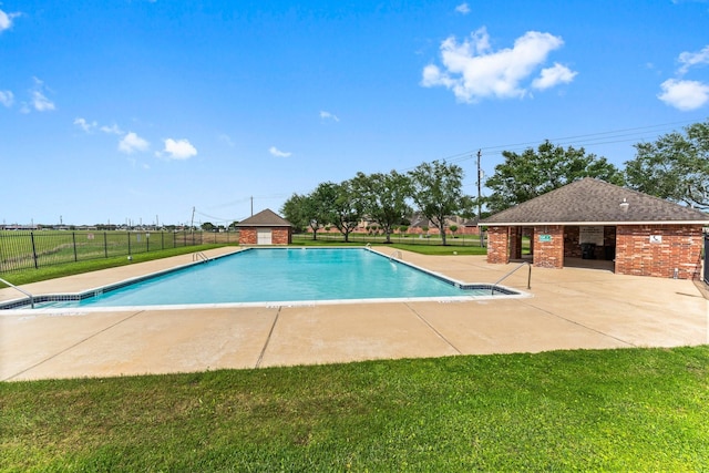community pool with fence, an outbuilding, a patio, and a lawn