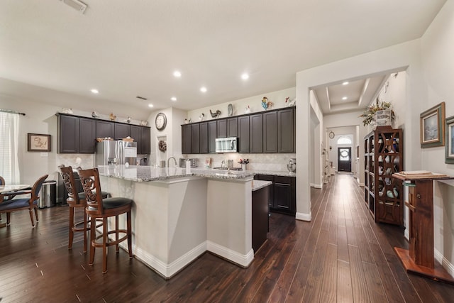 kitchen with backsplash, appliances with stainless steel finishes, light stone countertops, a spacious island, and dark wood-style floors