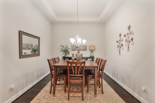 dining area featuring baseboards, wood finished floors, a tray ceiling, and an inviting chandelier