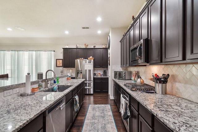 kitchen with dark wood-style flooring, light stone counters, a sink, backsplash, and stainless steel appliances