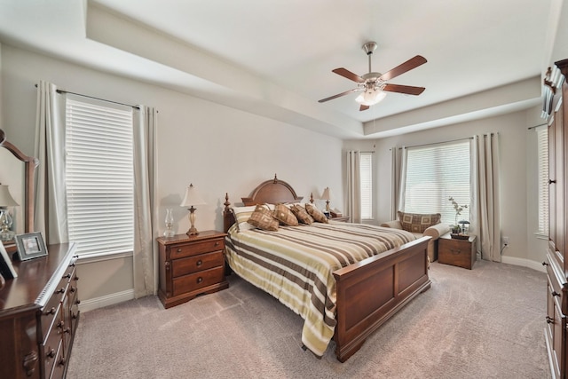 bedroom featuring a ceiling fan, baseboards, light colored carpet, and a tray ceiling