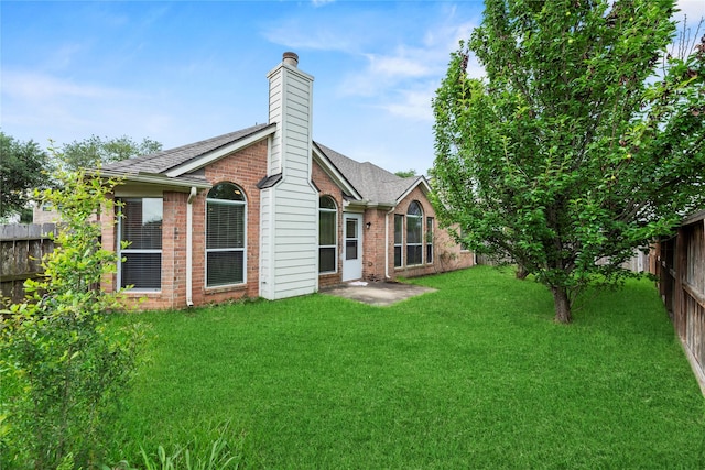 back of property featuring a shingled roof, brick siding, a fenced backyard, a chimney, and a lawn