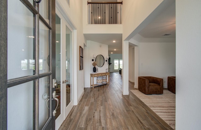 entryway with french doors, baseboards, wood finished floors, a towering ceiling, and visible vents