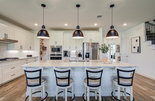 kitchen featuring visible vents, under cabinet range hood, a sink, light wood finished floors, and stainless steel appliances