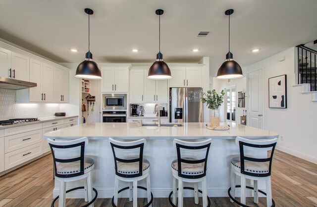 19018 Valentine Padlock Cir, Tomball, TX 77377 - kitchen with stainless steel appliances, a sink, under cabinet range hood, light wood-style floors, and a spacious island