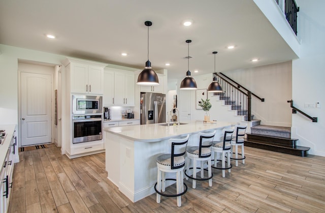 kitchen featuring a sink, appliances with stainless steel finishes, a center island with sink, and light wood finished floors