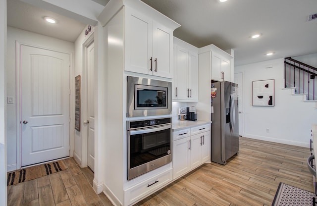 kitchen with white cabinets, light wood-style floors, light countertops, stainless steel appliances, and baseboards