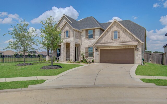 french provincial home with concrete driveway, fence, a shingled roof, and a front yard