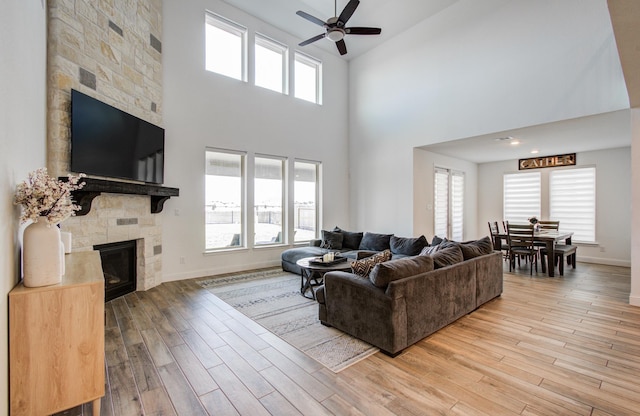living room with a ceiling fan, light wood-style flooring, a high ceiling, and a fireplace