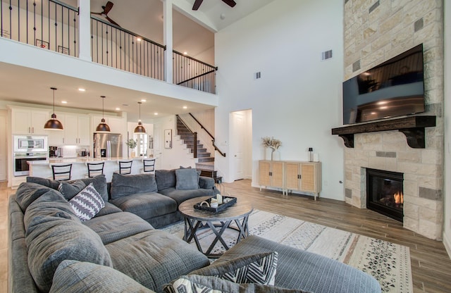 19018 Valentine Padlock Cir, Tomball, TX 77377 - living room featuring a fireplace, light wood finished floors, a high ceiling, ceiling fan, and stairs