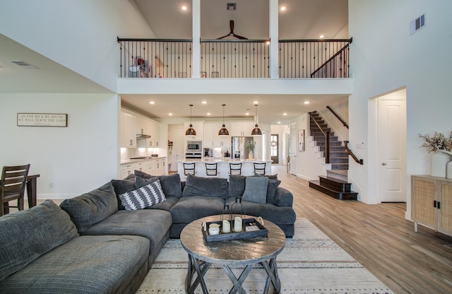 living room featuring stairs, light wood-style flooring, a high ceiling, and visible vents