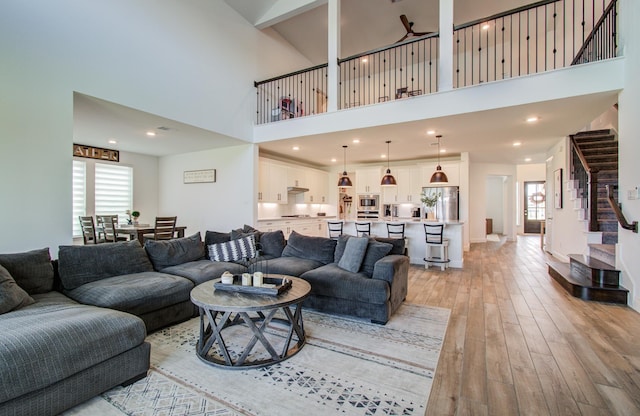 living room with plenty of natural light, light wood finished floors, stairs, and a towering ceiling