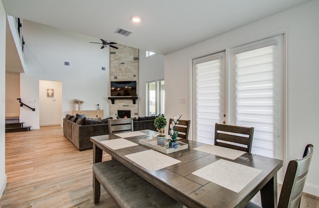 dining room featuring ceiling fan, a stone fireplace, light wood-type flooring, visible vents, and stairway