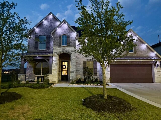 french country style house with concrete driveway, a front lawn, stone siding, and a standing seam roof