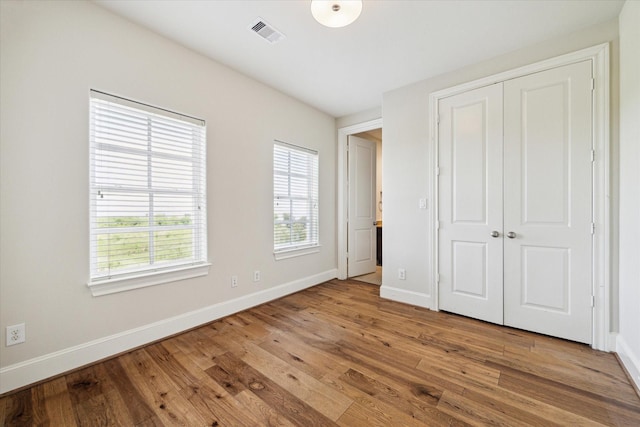 unfurnished bedroom featuring baseboards, visible vents, wood finished floors, and a closet