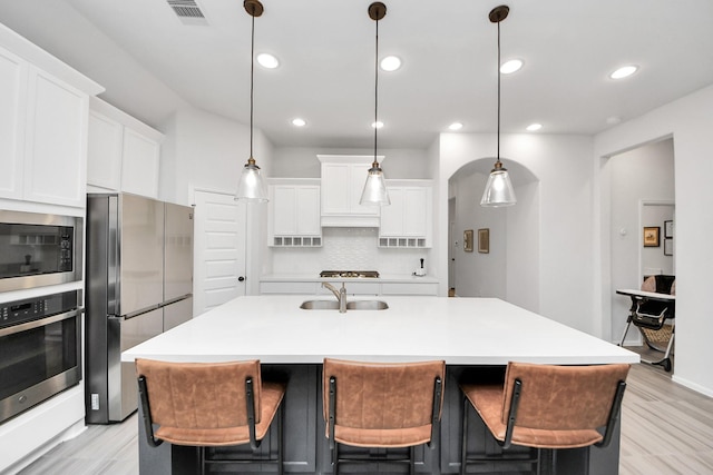 kitchen with decorative backsplash, an island with sink, light wood-type flooring, a sink, and appliances with stainless steel finishes