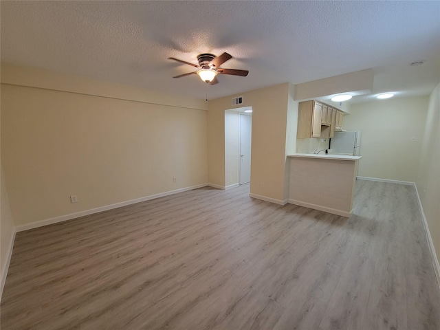 unfurnished living room with light wood finished floors, a textured ceiling, a ceiling fan, baseboards, and visible vents