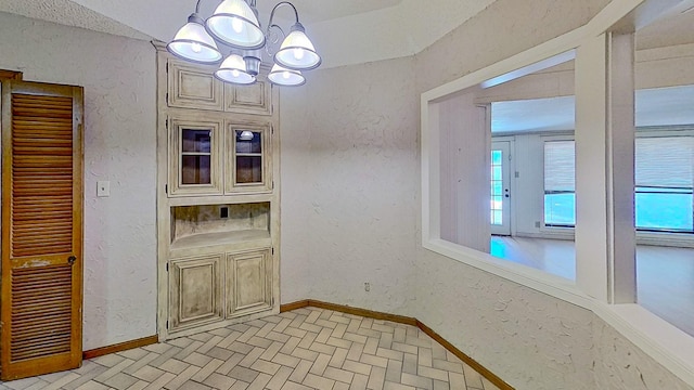 unfurnished dining area featuring baseboards, a notable chandelier, brick patterned floor, and a wealth of natural light