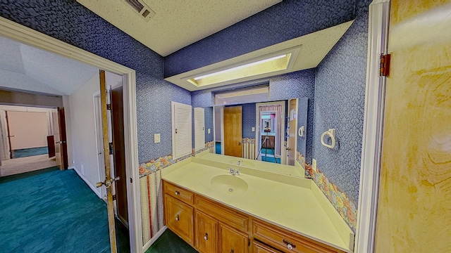 bathroom featuring vanity, a textured ceiling, visible vents, and wallpapered walls