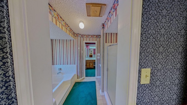 full bath featuring a textured ceiling, tile patterned floors, wallpapered walls, a garden tub, and a stall shower