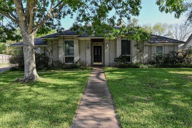 ranch-style home featuring a shingled roof and a front lawn