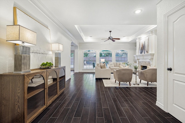 living room with crown molding, wood finished floors, a fireplace, ceiling fan, and a tray ceiling