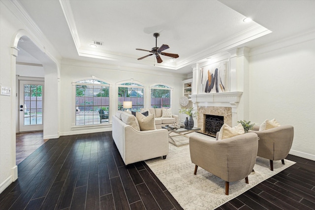 living area with ceiling fan, a raised ceiling, a premium fireplace, dark wood finished floors, and ornamental molding