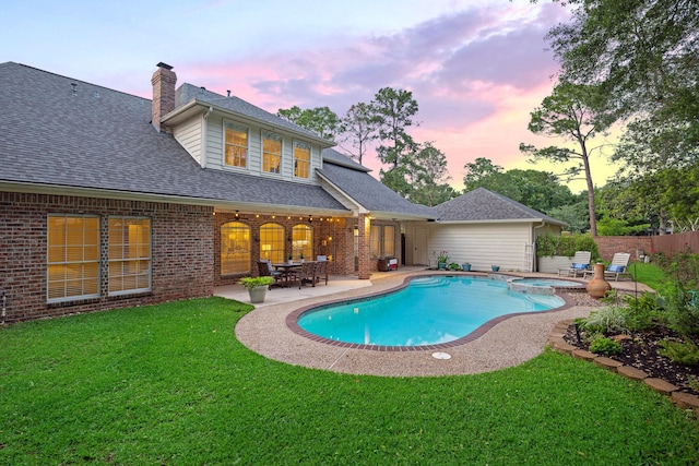 pool at dusk featuring a yard, a pool with connected hot tub, fence, and a patio area