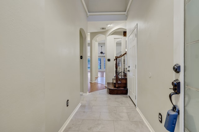 hall with visible vents, ornamental molding, baseboards, stairway, and arched walkways