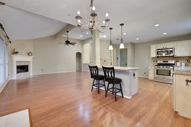 kitchen with a peninsula, a kitchen bar, arched walkways, light wood finished floors, and appliances with stainless steel finishes