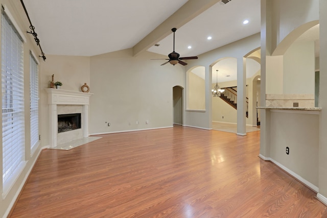 unfurnished living room featuring lofted ceiling with beams, ceiling fan, a high end fireplace, arched walkways, and light wood finished floors