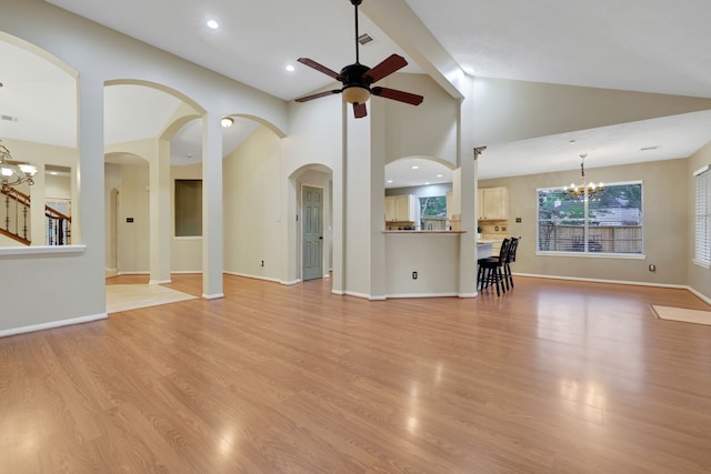 unfurnished living room featuring light wood finished floors, arched walkways, ceiling fan with notable chandelier, baseboards, and vaulted ceiling