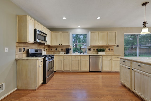 kitchen with backsplash, appliances with stainless steel finishes, a sink, light wood-style floors, and light brown cabinets