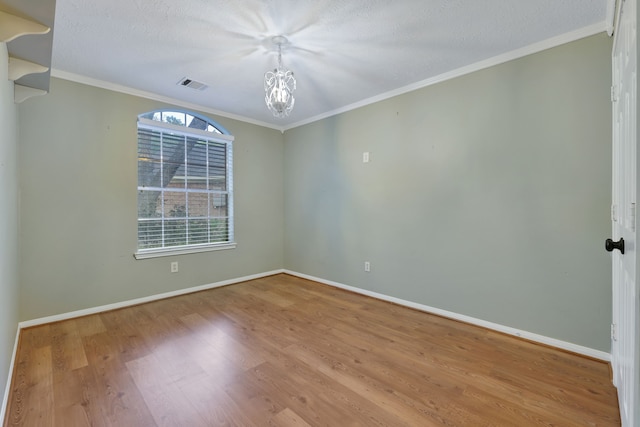 unfurnished room with crown molding, an inviting chandelier, baseboards, wood finished floors, and visible vents