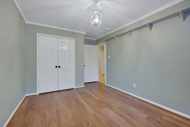 unfurnished bedroom featuring baseboards, a chandelier, ornamental molding, and light wood finished floors