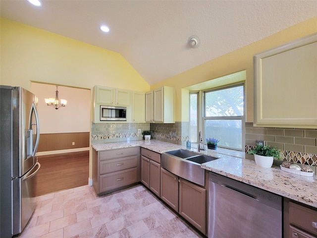 kitchen with light stone countertops, appliances with stainless steel finishes, a sink, decorative backsplash, and lofted ceiling
