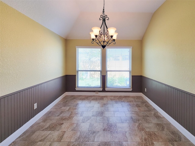 unfurnished dining area with a textured wall, a chandelier, and lofted ceiling