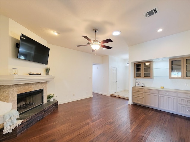 unfurnished living room with visible vents, dark wood-style flooring, baseboards, ceiling fan, and a fireplace with raised hearth