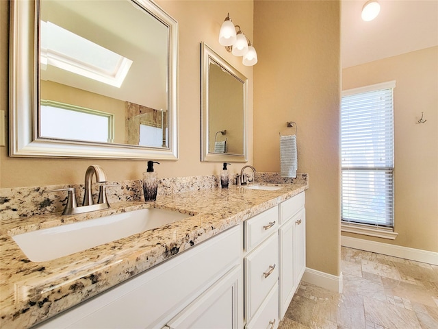 bathroom featuring baseboards, a sink, double vanity, and a skylight