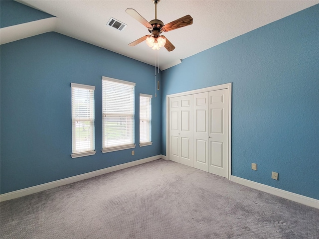 unfurnished bedroom with ceiling fan, carpet floors, vaulted ceiling, visible vents, and a closet
