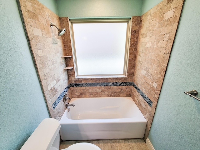 full bath featuring toilet, a textured wall, and a bath