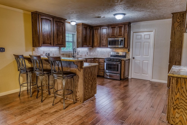 kitchen featuring a breakfast bar area, stainless steel appliances, a peninsula, wood finished floors, and tasteful backsplash
