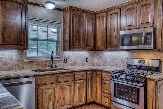 kitchen with light stone counters, a sink, decorative backsplash, and stainless steel appliances