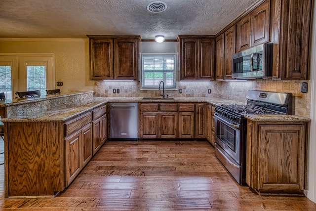 kitchen with a sink, appliances with stainless steel finishes, a peninsula, and hardwood / wood-style flooring