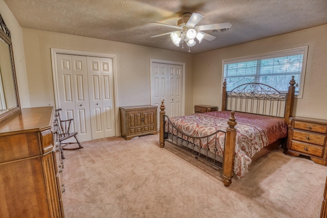 carpeted bedroom with visible vents, a textured ceiling, multiple closets, and ceiling fan