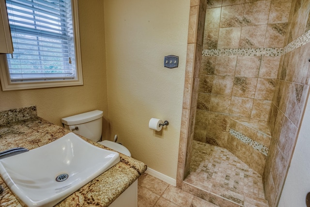 bathroom featuring tile patterned flooring, a tile shower, a sink, baseboards, and toilet