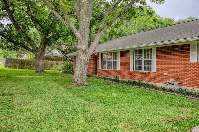 view of side of home with fence, a yard, roof with shingles, and brick siding
