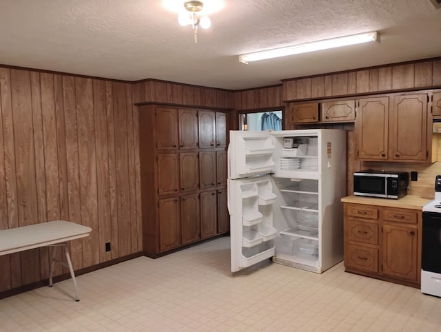 kitchen featuring light countertops, a textured ceiling, stainless steel microwave, and freestanding refrigerator